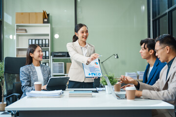 Fototapeta premium In a boardroom, an Asian team meets at a desk, presenting financial terms and strategies. Executives and employees collaborate, sharing ideas and work guidelines for success during an annual meeting.