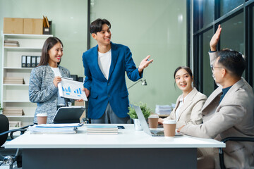 In a boardroom, an Asian team meets at a desk, presenting financial terms and strategies. Executives and employees collaborate, sharing ideas and work guidelines for success during an annual meeting.