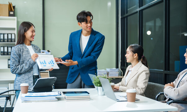 In a boardroom, an Asian team meets at a desk, presenting financial terms and strategies. Executives and employees collaborate, sharing ideas and work guidelines for success during an annual meeting. - Powered by Adobe