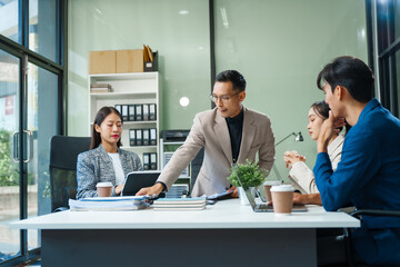 In a boardroom, an Asian team meets at a desk, presenting financial terms and strategies. Executives and employees collaborate, sharing ideas and work guidelines for success during an annual meeting.