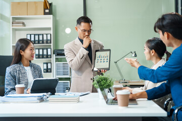 In a boardroom, an Asian team meets at a desk, presenting financial terms and strategies. Executives and employees collaborate, sharing ideas and work guidelines for success during an annual meeting.