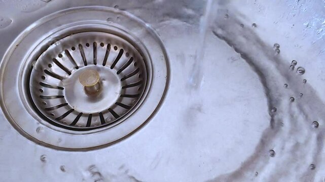 Plano corto de agua de un grifo corriendo por el desag&uuml;e en un fregadero de acero inoxidable o pila de la cocina