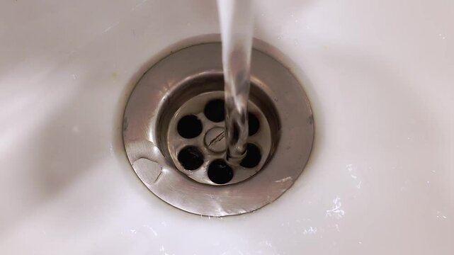 Plano corto de agua de un grifo corriendo por el desag&uuml;e en un fregadero o pila de la cocina