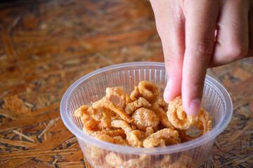 Close up of hand picking a Pork snack, Pork rind, Pork scratching or crackling in bowl on wooden background, Thai food, Thai stys, Eat with noodles.