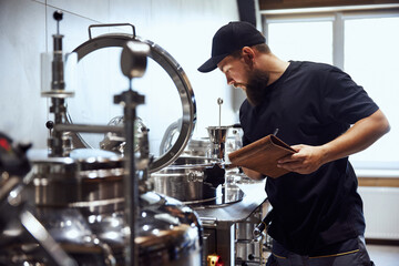 Bearded man, technologist checking brewing tools, making notes, demonstrating expertise needed to crafting beer. Concept of beer, brewery, manufacture, quality control