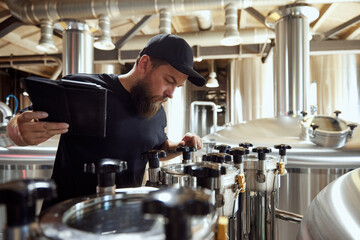 Focused and attentive man, brewery technologist adjusting valves and gauges, embodying expertise required in modern beer making. Concept of beer, brewery, manufacture, quality control