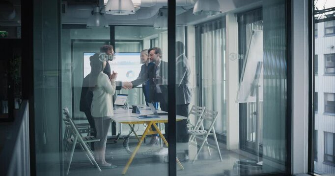 Multiethnic Group Having a Business Meeting in a Conference Room. Young People Looking at Analytical Data on Screen. Participants Agree on a Deal, Shake Hands and Celebrate a Successful Investment