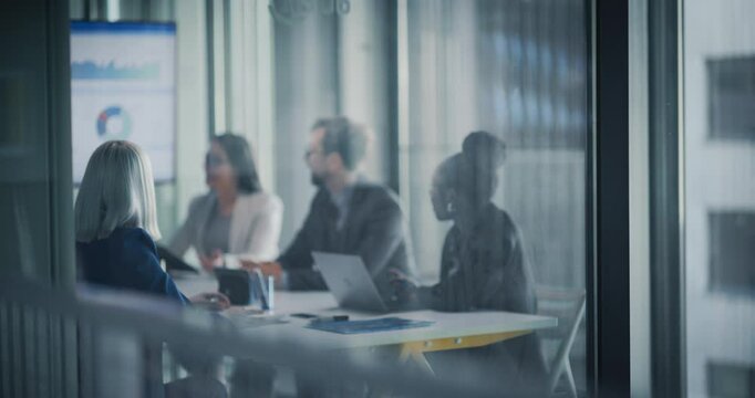 Diverse Team Engages in a Collaborative Strategic Planning Meeting in a Modern Glass-walled Conference Room. Office People Using Laptops and a Digital Whiteboard with Analytical Data