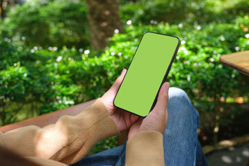 Mockup image of a woman holding mobile phone with blank desktop screen in the outdoors