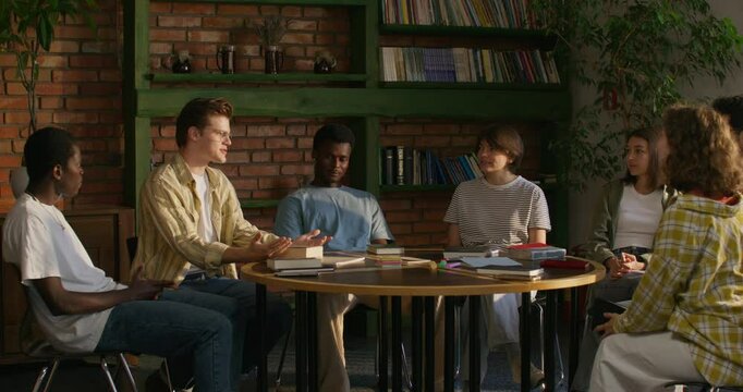 A man is talking to his friends while sitting at a table indoors. He opens the Bible. Bible Study Club