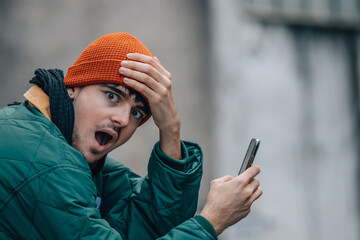 portrait of young man with hat and warm clothes looking at mobile phone surprised