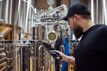 Concentrated man, technologist examining brewing equipment, maintaining thigh standards necessary for quality beer production. Concept of beer, brewery, manufacture, quality control