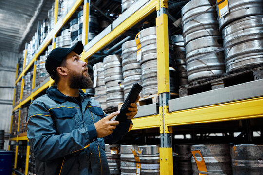 Brewery technologist inspecting rows of kegs in the storage area, getting ready for distribution. Maintaining accuracy in inventory tracking. Concept of beer, brewery, quality control