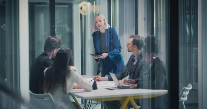 Group of Corporate Partners Analyzing Results From a Marketing Campaign. Project Manager Presenting Data, Employees Having a Conversation in a Meeting Room. View from Outside the Glass Room