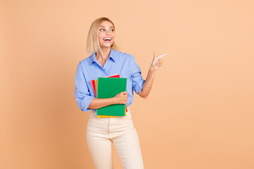 Photo of adorable lovely girl wear blue shirt holding copybooks looking showing empty space isolated beige color background