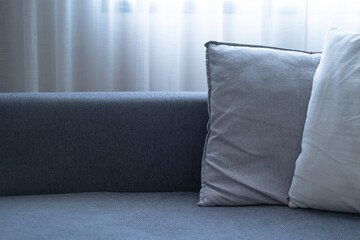 Close-up of cushions on cozy grey sofa. Modern interior of living room. with large window and sheer curtain.