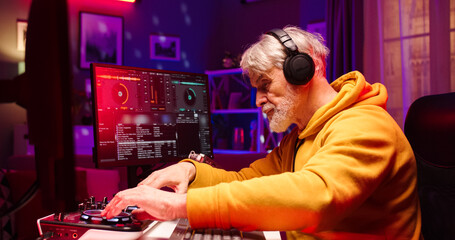 Close up portrait of old Caucasian male wearing headphones creates new modern music using DJ equipment. Handsome bearded face man works in room illuminated by LED light.