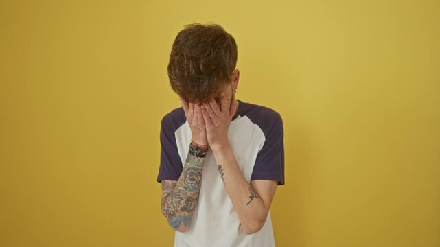 Young hispanic man standing alone, covering faces with hands and crying - a depictive study of depression and sad expression over an isolated yellow background
