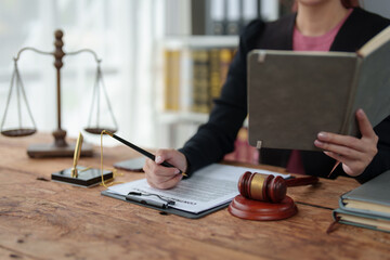 Asian female lawyer, law adviser, businessman looking through the law Business deal in the book working with the scales of the god of justice justice law concept.