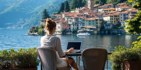 A woman works on a laptop at a table overlooking Lake Como in Italy.
