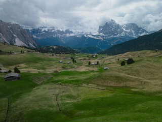 Big green meadow with little cabins surrounded by snowed mountains on the background in The Dolomites, Italy