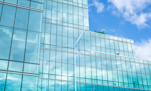 Green corporate building with wind turbine shadow cast on glass facade. Sustainable energy and efficient architectural design. Eco-friendly and modern urban development. Sustainable economic growth.