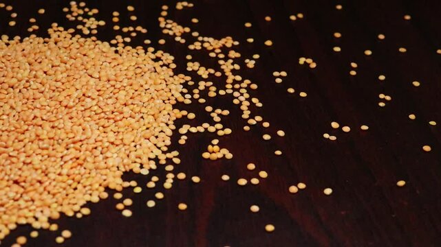 Masoor Dal, pulse, and pea are scattered on a black table. lentils falling from a jute sack. Organic orange-colored seeds, healthy lifestyle, high protein product concept.