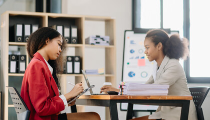 Business African women work and discuss their business plans. A Human employee explains and shows her colleague the results paper in office..