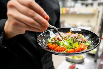 close-up of hands holding black bowl with fresh salad, featuring mixed greens, cherry tomatoes, and vegetables. vibrant colors and healthy ingredients make it perfect for food and lifestyle themes.