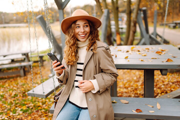 A young woman enjoying a peaceful autumn day outdoors, sitting at a table with her phone surrounded by colorful leaves