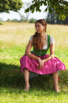 "Nachdenkliche Frau im Dirndl auf einer Wiese"