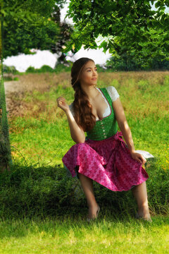 "Junge Frau im Dirndl auf einer gr&uuml;nen Wiese unter einem Baum"