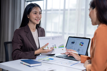 Two businesswomen analyzing financial charts on paper reports and digital tablet in office meeting