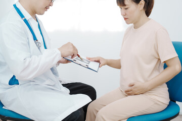 Asian female doctor listens to belly of pregnant mother during a prenatal exam in clinic. doctor provides caring advice, ensuring the health and happiness of the expecting mother and baby.