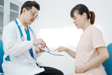 Fototapeta premium Asian female doctor listens to belly of pregnant mother during a prenatal exam in clinic. doctor provides caring advice, ensuring the health and happiness of the expecting mother and baby.