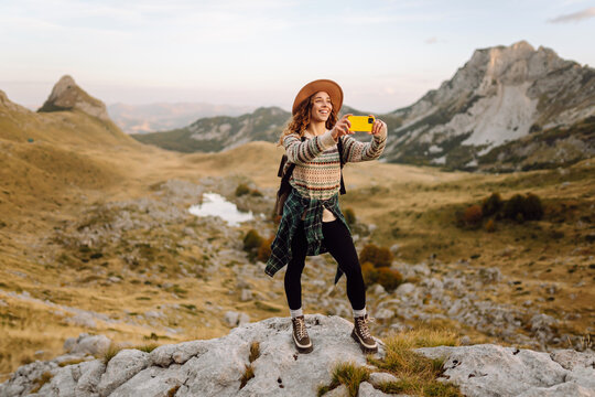 A young woman captures a moment while hiking in a mountainous landscape during golden hour