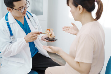 Asian female doctor listens to belly of pregnant mother during a prenatal exam in clinic. doctor provides caring advice, ensuring the health and happiness of the expecting mother and baby.