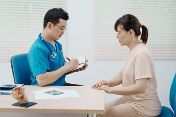 Obraz premium Asian female doctor listens to belly of pregnant mother during a prenatal exam in clinic. doctor provides caring advice, ensuring the health and happiness of the expecting mother and baby.
