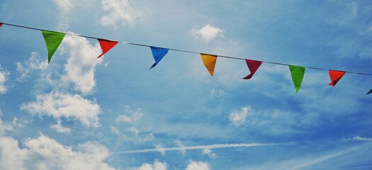 Colorful triangular pennant flags or bunting flags strung across a blue sky with clouds 