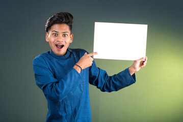 A happy young man is holding and displaying a signboard or placard on a dark background.