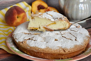 Fresh baked homemade charlotte pie sprinkled with powdered sugar. Slice of cake on metal shovel, peach halves, juicy peach fruit, striped yellow and white napkin. Close up view.