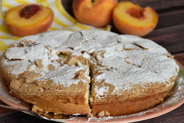 Fresh baked homemade charlotte pie sprinkled with powdered sugar. Slice of cake on metal shovel, peach halves, juicy peach fruit, striped yellow and white napkin. Close up view.