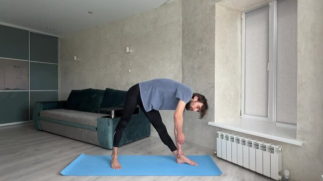 Young man practicing yoga, holding a variation of the extended triangle pose in his living room