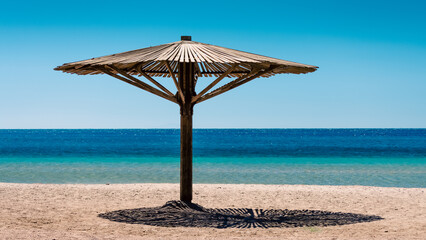 one wooden beach umbrella on the sand on the beach against the blue water of the Red Sea in Egypt Dahab South Sinai