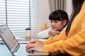 Mother working on laptop with daughter studying nearby