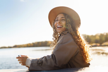 Young woman enjoying coffee outdoors while using smartphone in a sunny park during autumn