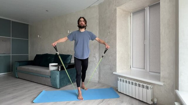Sportsman performing a lateral raise with a resistance band in an apartment, showcasing effective home workout techniques