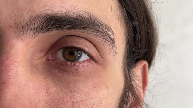 Eye close up. Man with long hair raises his eyebrows repeatedly against a clean white background, showcasing various facial expressions