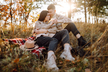 A young couple enjoying a romantic walk in the autumn forest, surrounded by fall foliage during sunset