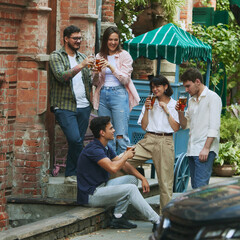 Good conversation and refreshing drinks. Young people, friends meeting at outdoor bar, pub, enjoying beer and lively atmosphere of weekend relaxation. Concept of relaxation, party, beer, party